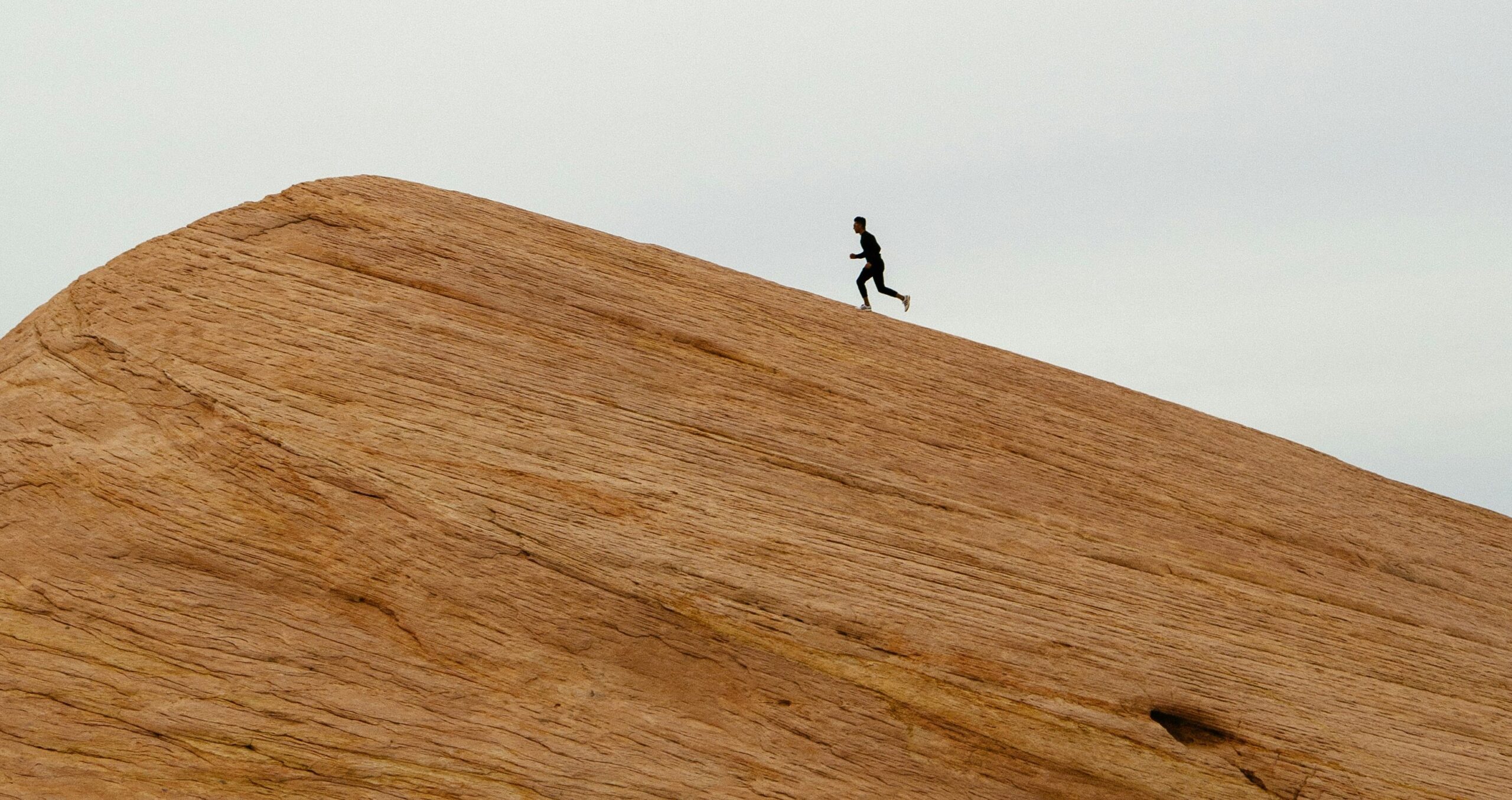 a person walking up a rock with grey blue sky in the background